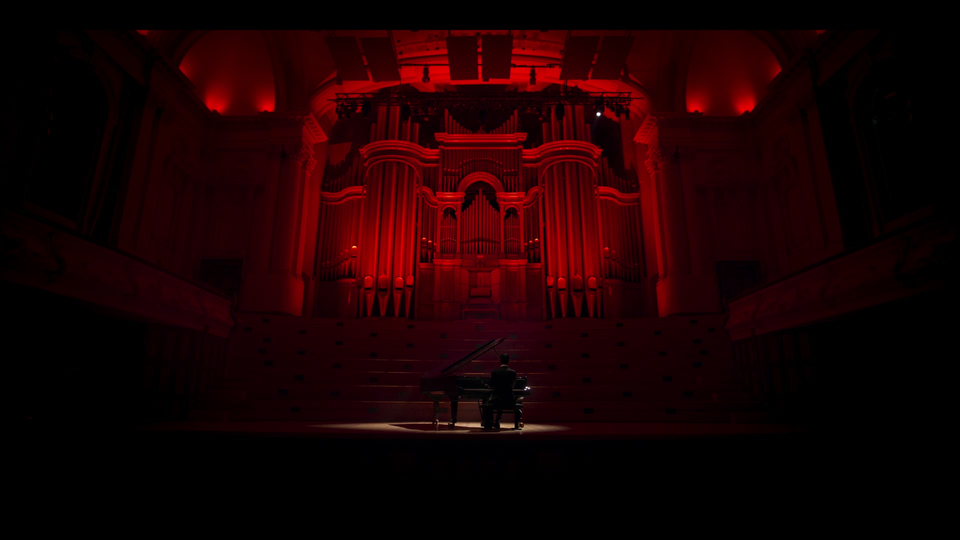 A pianist at a grand piano in a red-lit concert hall